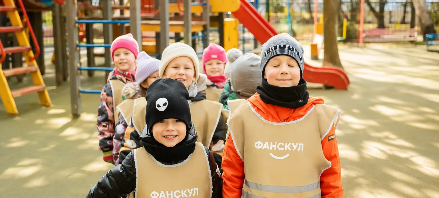 Дети детского сада Фанскул в фирменных жилетах на прогулке на площадке